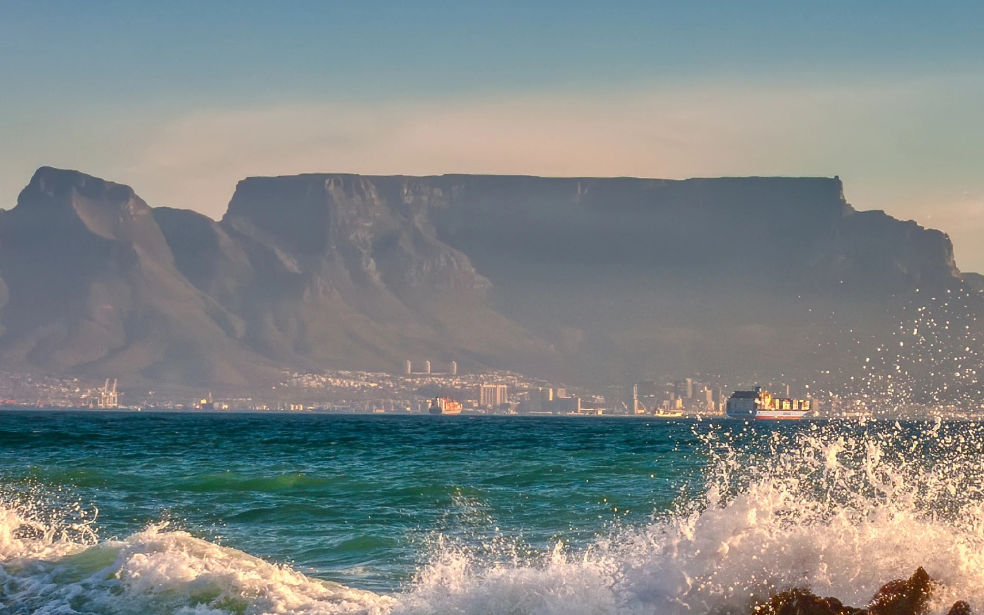 Table Mountain across Table Bay, with waves breaking over rocks in the foreground