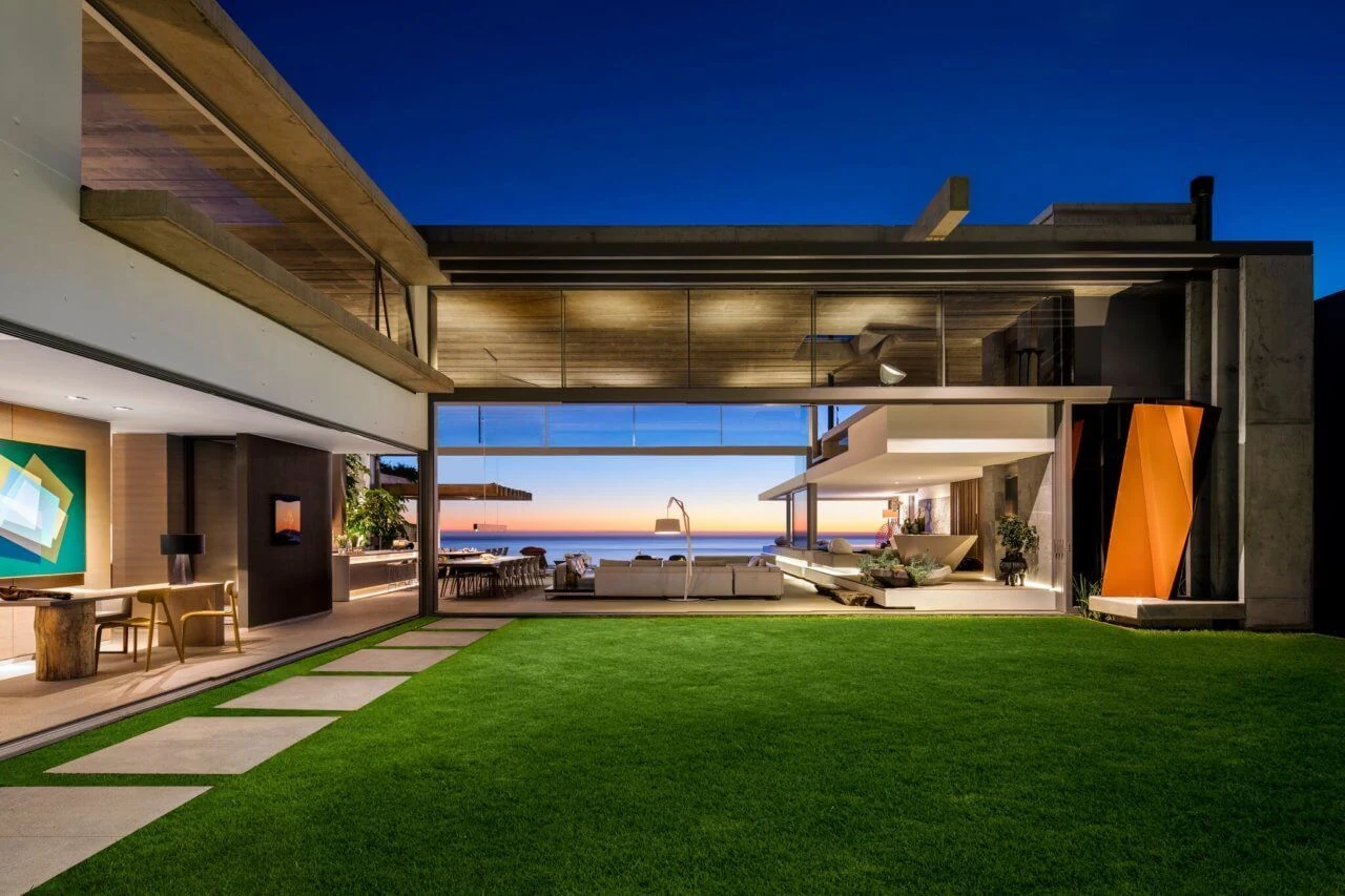 Modern private villa at dusk, with a lawn and an open-plan living area facing the ocean sunset