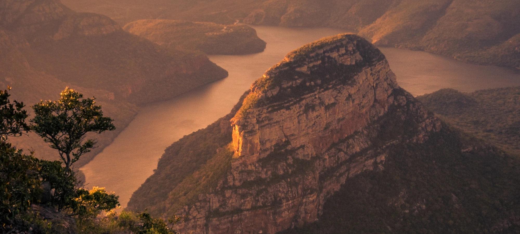 Blyde River Canyon at sunset, with the river curving between steep sandstone cliffs and wooded slopes