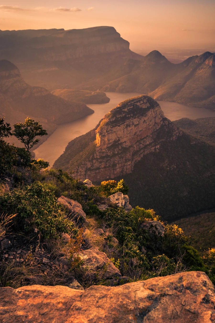 Blyde River Canyon at sunset, with the river winding between sandstone cliffs and a rocky ledge in the foreground