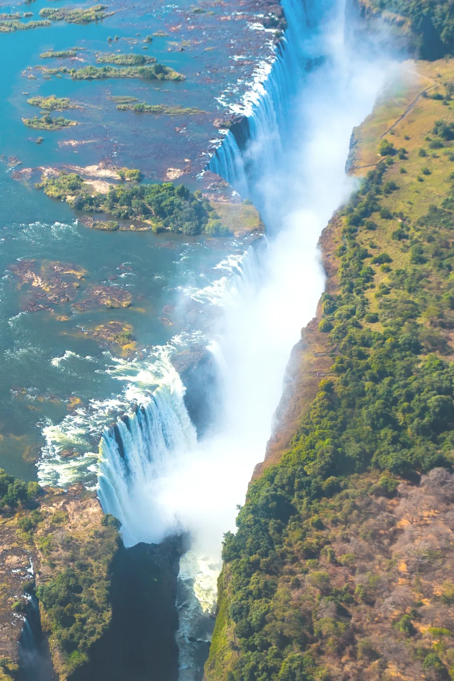 Aerial view of Victoria Falls, with spray rising from the gorge between green riverbanks