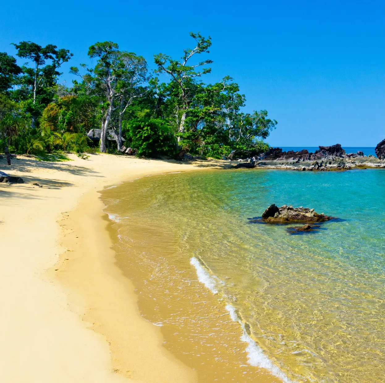 Quiet sandy beach with clear shallow water and forested rocks on the Madagascar coast